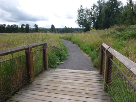 Transition from wooden bridge with railing onto compact gravel trail – may have a lip – bridge may be slick when wet